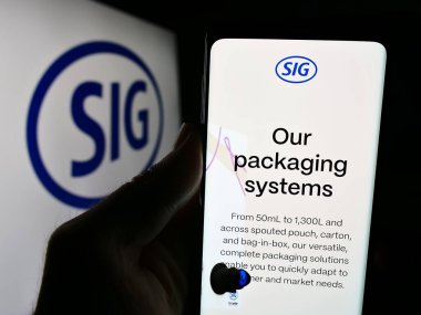 Stuttgart, Almanya - 05-31-2024: İsviçreli ambalaj şirketi SIG Group AG 'nin web sitesi ile iş logosu önünde cep telefonu tutan kişi. Telefon ekranının merkezine odaklan.