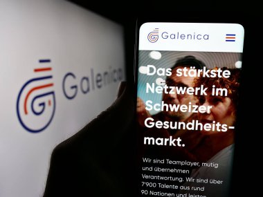Stuttgart, Almanya - 05-31-2024: İsviçreli ilaç şirketi Galenica AG 'nin internet sitesi ile iş logosu önünde cep telefonu tutan kişi. Telefon ekranının merkezine odaklan.