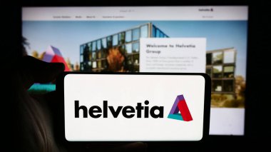 Stuttgart, Almanya - 05-31-2024: İsviçreli sigorta şirketi Helvetia Holding AG 'nin logosuyla cep telefonu tutan kişi iş sayfasının önünde. Telefon ekranına odaklan.