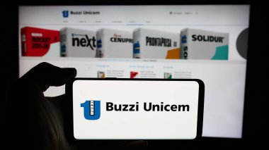 Stuttgart, Almanya - 06-01-2024: İtalyan inşaat malzemeleri şirketi Buzzi Unicem SpA 'nın logosuyla cep telefonu tutan kişi iş sayfasının önünde. Telefon ekranına odaklan.