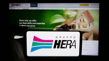 Stuttgart, Almanya - 06-01-2024: İtalyan hizmet şirketi Hera S.P.A 'nın logosuyla cep telefonu tutan kişi iş sayfasının önünde. Telefon ekranına odaklan.