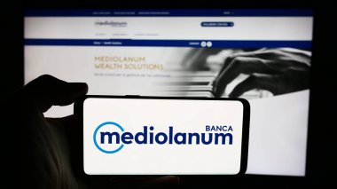 Stuttgart, Almanya - 06-01-2024: İtalyan finans şirketi Banca Mediolanum S.p.A. 'nın logosuyla cep telefonu tutan kişi iş sayfasının önünde. Telefon ekranına odaklan.