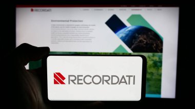 Stuttgart, Almanya - 06-01-2024: İtalyan ilaç şirketi Recordati S.p.A. 'nın logosunun bulunduğu cep telefonu sahibi kişi iş sayfasının önünde. Telefon ekranına odaklan.