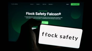 Stuttgart, Germany - 06-03-2024: Person holding cellphone with logo of US video surveillance company Flock Safety in front of business webpage. Focus on phone display. clipart