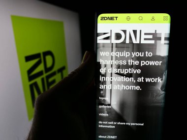 Stuttgart, Almanya - 06-03-2024: ABD 'li iş teknolojileri haber şirketi ZDNET' in web sitesi ile birlikte iş logosu önünde cep telefonu tutan kişi. Telefon ekranının merkezine odaklan.