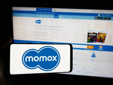 Stuttgart, Almanya - 03-06-2024: İnternet sitesinin önünde Alman yeniden ticaret şirketi Momox SE 'nin logosuna sahip kişi. Telefon ekranına odaklan.