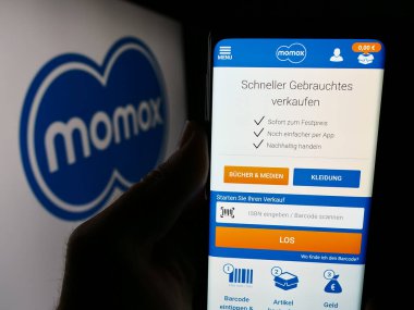 Stuttgart, Almanya - 03-06-2024: Alman yeniden ticaret şirketi Momox SE 'nin web sayfası ile birlikte iş logosu önünde cep telefonu tutan kişi. Telefon ekranının merkezine odaklan.