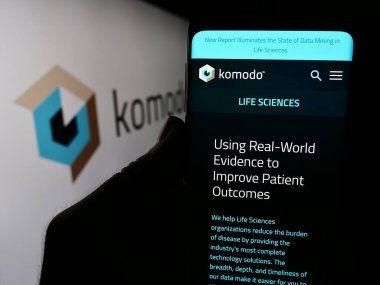 Stuttgart, Almanya - 03-06-2024: ABD 'li sağlık haritası şirketi Komodo Health Inc.' in web sayfası ile logo önünde akıllı telefon tutan kişi. Telefon ekranının merkezine odaklan.