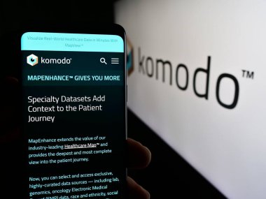 Stuttgart, Almanya - 03-06-2024: ABD 'li sağlık haritası şirketi Komodo Health Inc.' in internet sayfası ile logo önünde cep telefonu tutan kişi. Telefon ekranının merkezine odaklan.