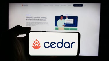 Stuttgart, Almanya - 03-06-2024: ABD 'li sağlık yazılım şirketi Cedar Cares Inc.' in logosuna sahip cep telefonu sahibi kişi iş sayfasının önünde. Telefon ekranına odaklan.