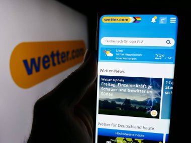 Stuttgart, Almanya - 06-06-2024: Alman hava portalı Wetter.com GmbH 'nin web sayfası ile logo önünde akıllı telefon tutan kişi. Telefon ekranının merkezine odaklan.