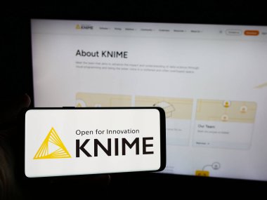 Stuttgart, Almanya - 06-06-2024: Üzerinde analitik yazılım şirketi KNIME AG 'nin logosu bulunan cep telefonu sahibi kişi iş sayfasının önünde. Telefon ekranına odaklan.