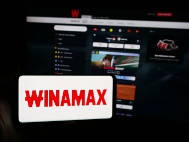 Stuttgart, Germany - 06-06-2024: Person holding mobile phone with logo of French sports betting company Winamax SA in front of business web page. Focus on phone display. clipart