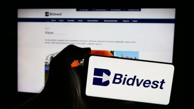 Stuttgart, Almanya - 06-07-2024: Güney Afrikalı holding Bidvest Group Limited 'in logosuna sahip cep telefonu sahibi kişi web sayfasının önünde. Telefon ekranına odaklan.