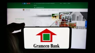 Stuttgart, Germany - 06-07-2024: Person holding cellphone with logo of Bangladeshi microfinance company Grameen Bank in front of business webpage. Focus on phone display. clipart