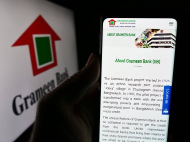 Stuttgart, Almanya - 06-07-2024: Bangladeş mikrofinans şirketi Grameen Bank 'ın internet sayfası ile logo önünde cep telefonu tutan kişi. Telefon ekranının merkezine odaklan.