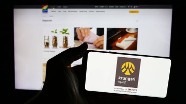 Stuttgart, Almanya - 06-07-2024: İnternet sitesi önünde üzerinde Ayudhya Devlet Şirketi Limited (Krungsri) logosu bulunan kişi. Telefon ekranına odaklan.