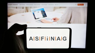 Stuttgart, Almanya - 06-11-2024: Avusturyalı otoyol altyapı şirketi ASFINAG 'ın logosuyla cep telefonu tutan kişi iş sayfası önünde. Telefon ekranına odaklan.