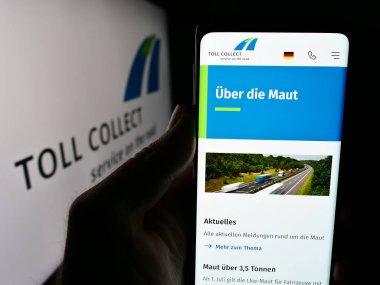 Stuttgart, Almanya - 06-11-2024: Alman otoban gişe sistemi şirketi Toll Collect GmbH 'in logolu web sayfası ile cep telefonu tutan kişi. Telefon ekranının merkezine odaklan.