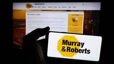 Stuttgart, Almanya - 06-11-2024: Güney Afrikalı Murray ve Roberts Holding Ltd. 'nin logosuna sahip cep telefonu sahibi kişi web sayfasının önünde. Telefon ekranına odaklan.