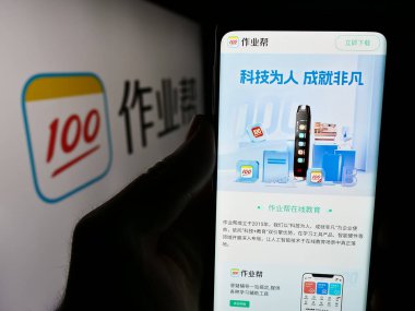 Stuttgart, Almanya - 06-11-2024: Çinli çevrimiçi eğitim platformu şirketi Zuoyebang 'ın internet sayfası ile logo önünde cep telefonu tutan kişi. Telefon ekranının merkezine odaklan.