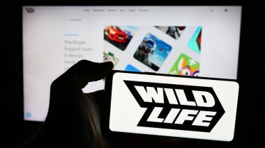 Stuttgart, Almanya - 06-11-2024: Brezilyalı oyun şirketi Wild Life Inc. (Vahşi Yaşam Stüdyoları) 'un logosunun bulunduğu cep telefonu sahibi kişi web sitesinin önünde. Telefon ekranına odaklan.