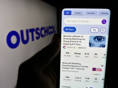 Stuttgart, Almanya - 06-12-2024: ABD 'li çevrimiçi eğitim şirketi Outschool Inc.' nin internet sayfası ile iş logosu önünde cep telefonu tutan kişi. Telefon ekranının merkezine odaklan.