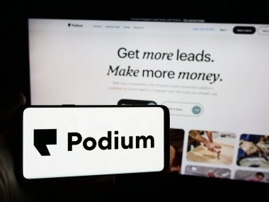 Stuttgart, Germany - 06-12-2024: Person holding mobile phone with logo of American software company Podium Corporation Inc. in front of business web page. Focus on phone display. clipart