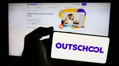Stuttgart, Almanya - 06-12-2024: Amerikan çevrimiçi eğitim şirketi Outschool Inc. 'nin logosuyla cep telefonu sahibi kişi iş sayfasının önünde. Telefon ekranına odaklan.
