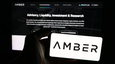 Stuttgart, Almanya - 06-13-2024: Kripto hizmet şirketi Amber Global Limited 'in logosuna sahip cep telefonu sahibi kişi iş sayfasının önünde. Telefon ekranına odaklan.
