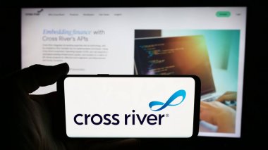 Stuttgart, Germany - 06-13-2024: Person holding cellphone with logo of US financial services company Cross River Bank in front of business webpage. Focus on phone display. clipart