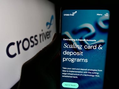 Stuttgart, Germany - 06-13-2024: Person holding smartphone with webpage of US financial services company Cross River Bank in front of logo. Focus on center of phone display. clipart