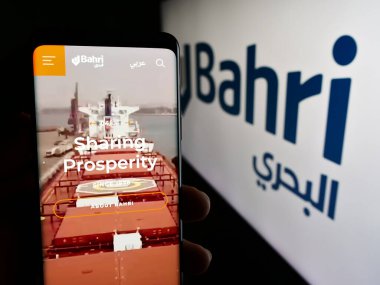 Stuttgart, Germany - 06-14-2024: Person holding cellphone with webpage of business National Shipping Company of Saudi Arabia (Bahri) in front of logo. Focus on center of phone display. clipart