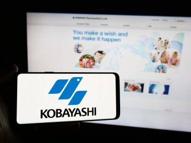 Stuttgart, Almanya - 06-24-2024: Japon şirketi Kobayashi Pharmaceutical Co. Ltd. nin logosuna sahip akıllı telefon sahibi kişi web sitesinin önünde. Telefon ekranına odaklan.