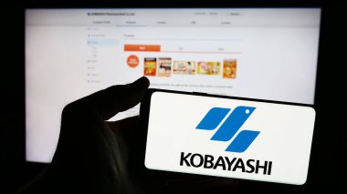 Stuttgart, Almanya - 06-24-2024: Japon şirketi Kobayashi Pharmaceutical Co. Ltd. 'nin logosunun bulunduğu cep telefonu sahibi kişi iş sayfasının önünde. Telefon ekranına odaklan.