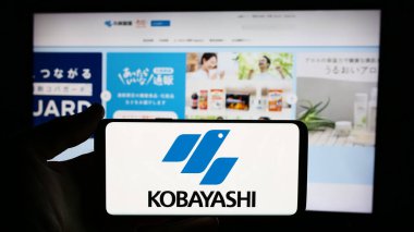 Stuttgart, Almanya - 06-24-2024: Japon şirketi Kobayashi Pharmaceutical Co. Ltd. 'nin logosuyla cep telefonu tutan kişi iş sayfasının önünde. Telefon ekranına odaklan.