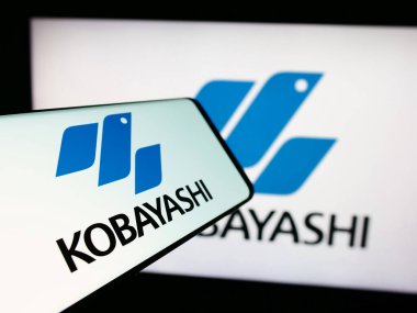 Stuttgart, Germany - 06-24-2024: Smartphone with logo of Japanese company Kobayashi Pharmaceutical Co. Ltd. in front of monitor. Focus on center-left of phone display. clipart