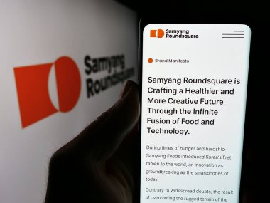 Stuttgart, Almanya - 06-24-2024: Güney Koreli gıda şirketi Samyang Roundsquare Co. Ltd. logolu akıllı telefon sahibi kişi. Telefon ekranının merkezine odaklan.