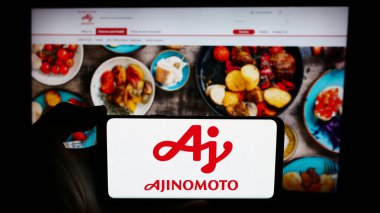 Stuttgart, Almanya - 06-24-2024: Japon gıda şirketi Ajinomoto Co. Inc. 'nin logosuna sahip cep telefonu sahibi kişi iş sayfasının önünde. Telefon ekranına odaklan.