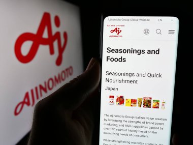 Stuttgart, Almanya - 06-24-2024: Japon gıda şirketi Ajinomoto Co. Inc. 'nin internet sayfası ile iş logosu önünde cep telefonu tutan kişi. Telefon ekranının merkezine odaklan.