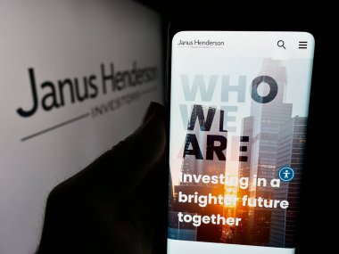 Stuttgart, Almanya - 06-25-2024: Logo önünde varlık yönetimi şirketi Janus Henderson Group plc 'nin web sitesi ile cep telefonu tutan kişi. Telefon ekranının merkezine odaklan.