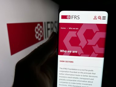 Stuttgart, Almanya - 06-26-2024: Uluslararası Mali Raporlama Standartları Vakfı (IFRS) web sitesi ile cep telefonu bulunduran kişi. Telefon ekranının merkezine odaklan.