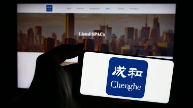 Stuttgart, Almanya - 06-26-2024: Yatırım şirketi Chenghe Group Ltd. 'nin logosuna sahip cep telefonu sahibi kişi iş sayfasının önünde. Telefon ekranına odaklan.