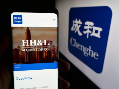 Stuttgart, Almanya - 06-26-2024: Yatırım şirketi Chenghe Group Ltd. 'nin web sayfası ile iş logosu önünde cep telefonu tutan kişi. Telefon ekranının merkezine odaklan.