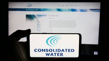 Stuttgart, Almanya - 06-26-2024: Deniz suyu arıtma şirketi Consolidated Water Co. Ltd. nin logosuna sahip cep telefonu sahibi kişi web sayfasının önünde. Telefon ekranına odaklan.