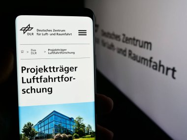 Stuttgart, Almanya - 06-26-2024: Deutsches Zentrum kürk Luft- und Raumfahrt e.V. sitesi ile akıllı telefon (DLR) Logonun önünde. Telefon ekranının sol üst kısmına odaklan.