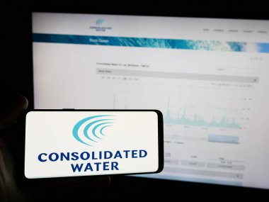 Stuttgart, Germany - 06-26-2024: Person holding mobile phone with logo of seawater desalination company Consolidated Water Co. Ltd. in front of web page. Focus on phone display. clipart