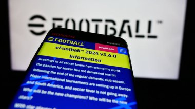 Stuttgart, Germany - 06-27-2024: Smartphone with website of football video game eFootball (Konami) in front of business logo. Focus on top-left of phone display. clipart