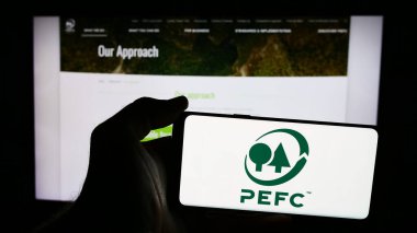 Stuttgart, Almanya - 06-27-2024: İnternet sayfası önünde Orman Onaylama Programı (PEFC) logosu bulunan kişi. Telefon ekranına odaklan.