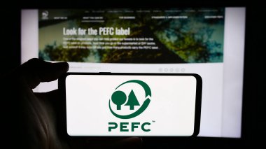 Stuttgart, Almanya - 06-27-2024: İnternet sayfası önünde Orman Onaylama Programı (PEFC) logosu bulunan kişi. Telefon ekranına odaklan.